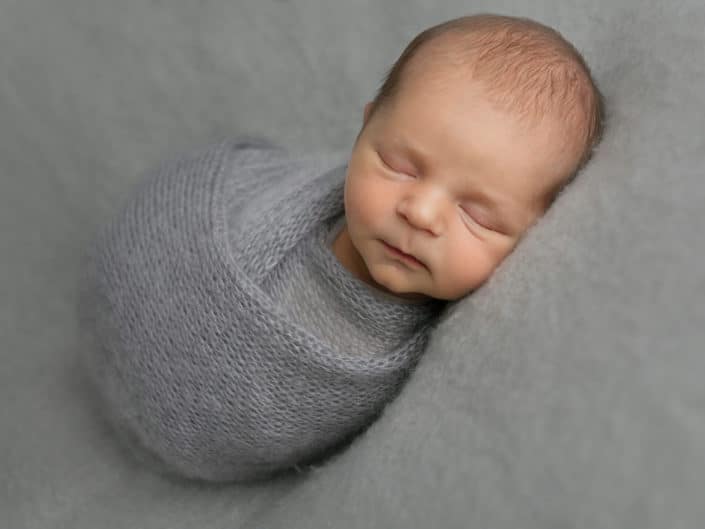 Newborn baby boy wrapped into grey wrap sleeping on his left side