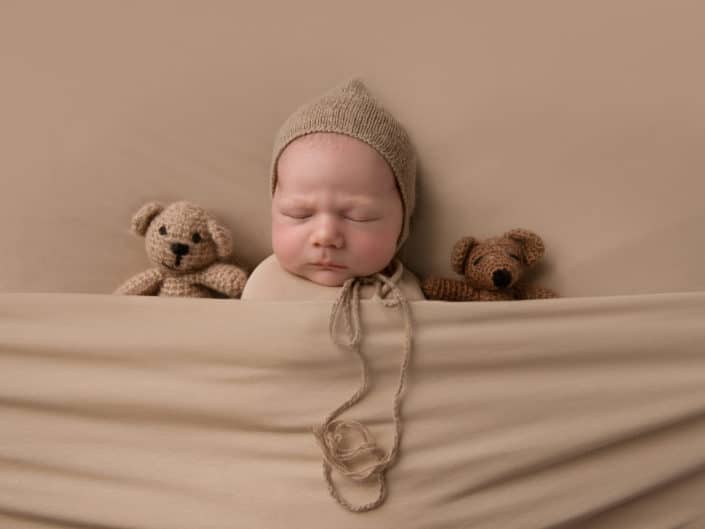 Vastasyntyneen poika vauva ruskeassa kapalossa ja hatussa nallen keskellä
