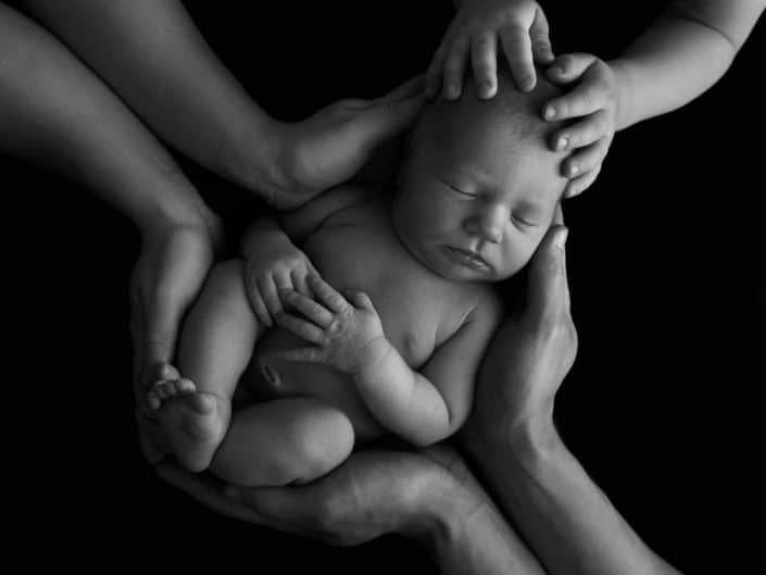 Newborn baby boy in his parent's and brother's hands