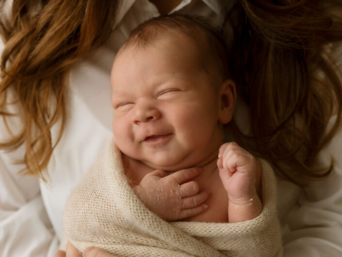 Vastasyntynyt vauva beige kapalossa hymyilemässä äidin sylissä