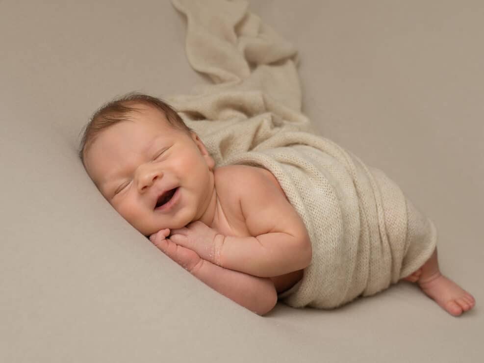 Vastasyntynyt vauva beige kapalossa nukkumassa ja hymyilemässä