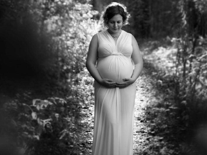 Pregnant woman in white dress in a forest on a black and white photo