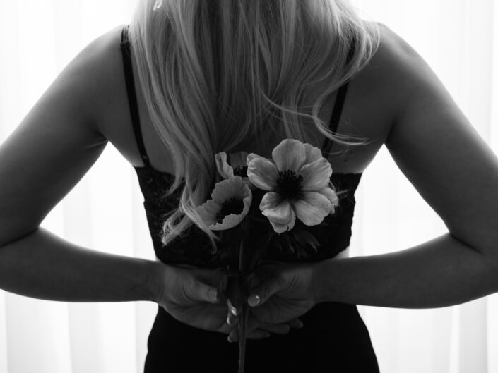 Vaaleatukkainen nainen seisomassa valon edessä ja pitämässä käsissä kukkia selän takana