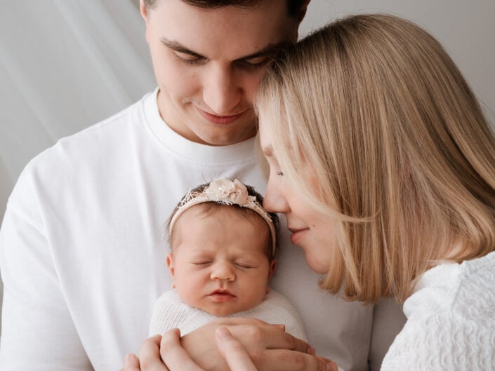 Jyväskylän perhekuvaus by Madlen Photography: valkoisiin vaatteisiin pukeutunut pariskunta pitelee valkoiseen peittoon käärittyä vastasyntynyttä vauvaa.