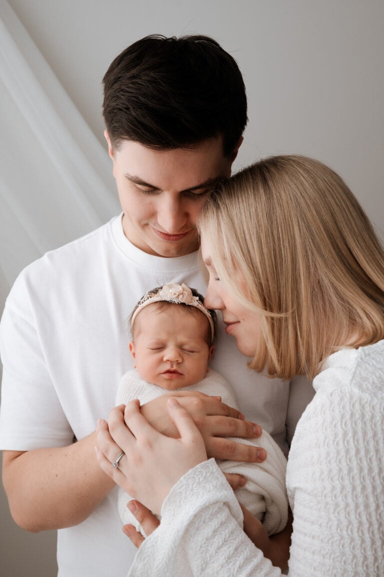 Jyväskylän perhekuvaus by Madlen Photography: valkoisiin vaatteisiin pukeutunut pariskunta pitelee valkoiseen peittoon käärittyä vastasyntynyttä vauvaa.