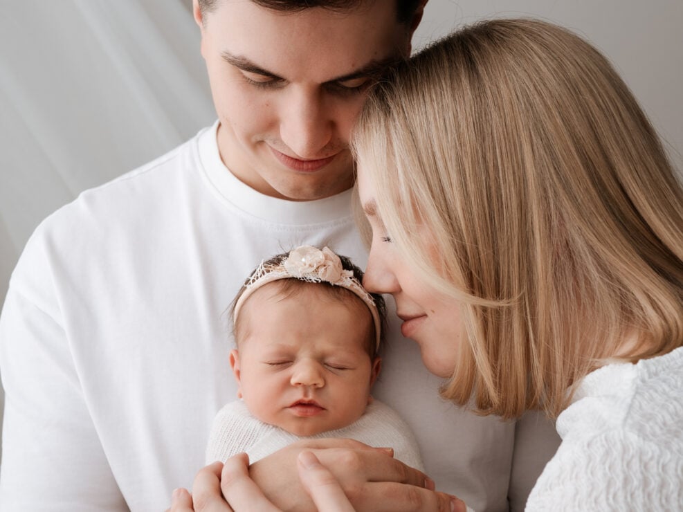 Jyväskylän perhekuvaus by Madlen Photography: valkoisiin vaatteisiin pukeutunut pariskunta pitelee valkoiseen peittoon käärittyä vastasyntynyttä vauvaa.