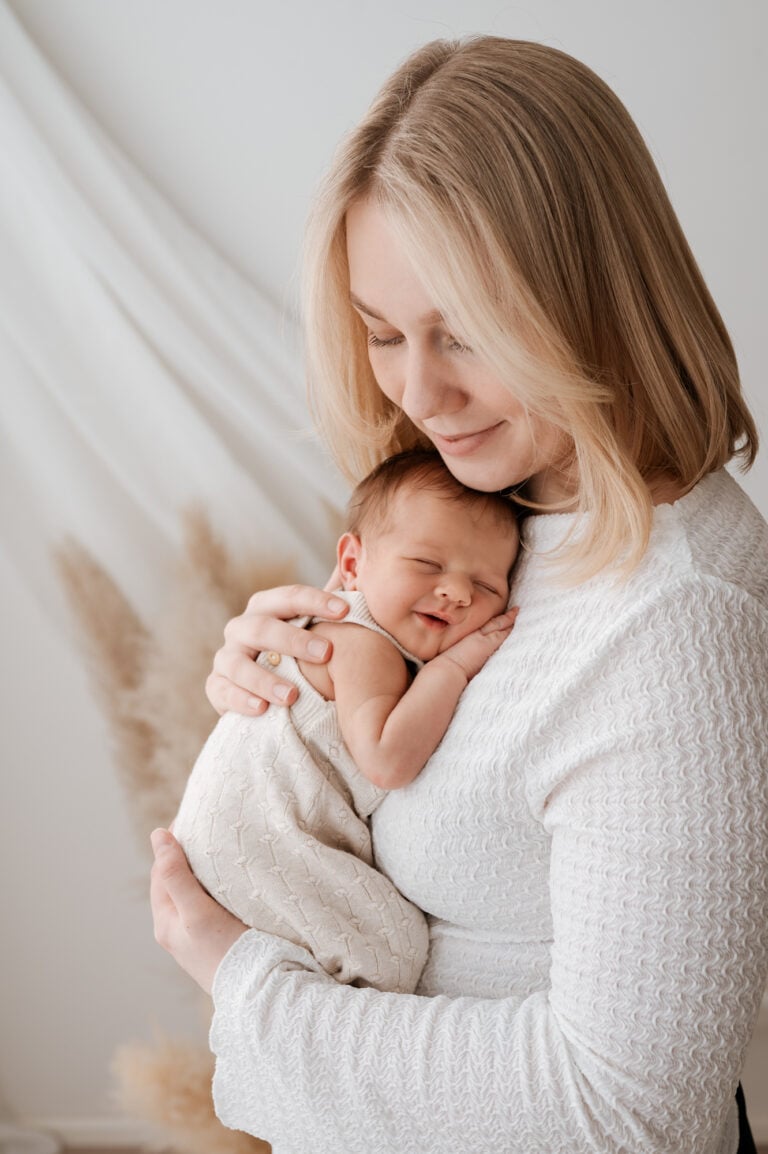 Vastasyntyneiden valokuvaus Jyväskylä: vaalea äiti pehmeässä valossa halailemassa nukkuvaa vauvaa, molemmilla vaaleat vaatteet, Madlen Photography.