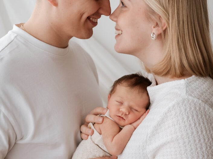 Onnellinen pariskunta Jyväskylässä pitelee nukkuvaa vastasyntynyttä valkoiseen peittoon käärittynä - kuvaaja Madlen Photography.