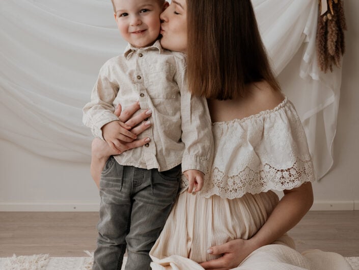 Jyväskylän perhekuva by Madlen Photography: nainen valkoisessa mekossa suutelee nuorta poikaa poskelle, molemmilla vaaleat asut.